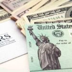 A tax refund check from the IRS alongside various denominations of cash