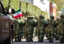 Soldiers in green camouflage march carrying rifles and a Mexican flag