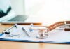 Stethoscope on a prescription form beside a pen and laptop