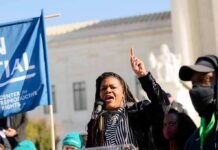 Dem Civil War Explodes In Missouri Woman speaking at a rally with raised finger and microphone