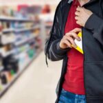 person concealing a small box inside a hoodie in a store aisle