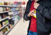 person concealing a small box inside a hoodie in a store aisle