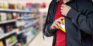 person concealing a small box inside a hoodie in a store aisle