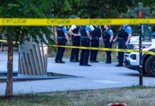 police officers stand behind caution tape at a park scene