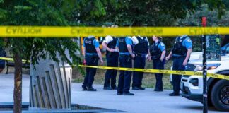 police officers stand behind caution tape at a park scene
