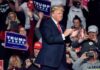 man in suit claps on stage at a rally