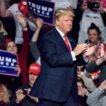 man in suit claps on stage at a rally