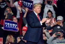 Trump Highlights Historic Crime Drop During Visit man in suit claps on stage at a rally