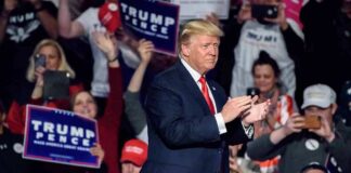 man in suit claps on stage at a rally