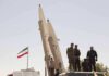 Iran Bounty Puts U.S. Troops in Crosshairs soldiers stand beside large missiles at outdoor display