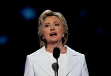 woman in white suit speaking at a microphone