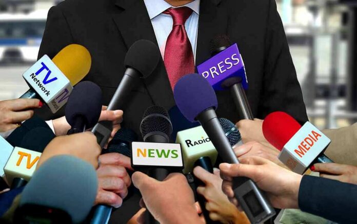 shutterstock_1096799972 Press microphones surround a suited spokesperson