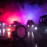 Handcuffs on a surface with police cars and flashing lights in the background