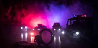 Handcuffs on a surface with police cars and flashing lights in the background