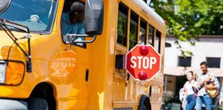 School bus with extended stop sign near students on sidewalk