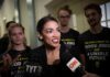 Dem Power Brokers Panic Over AOC Woman speaking to reporters with microphones surrounded by supporters