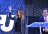 Melania Trump waves on stage beside Eric Bolling at an event