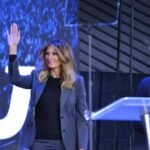 Melania Trump waves on stage beside Eric Bolling at an event