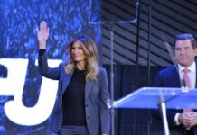Melania Trump waves on stage beside Eric Bolling at an event