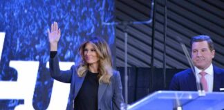 Melania Trump waves on stage beside Eric Bolling at an event