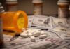 Prescription pill bottle and white tablets on scattered US dollar bills