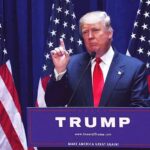 Energized Trump Stuns Prime-Time man in suit speaking at podium with multiple American flags