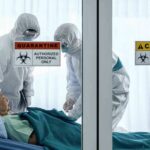 Healthcare workers in hazmat suits treat a patient in a quarantine room