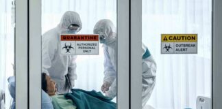Healthcare workers in hazmat suits treat a patient in a quarantine room