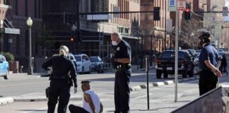 Police officers detain a seated man on a city sidewalk