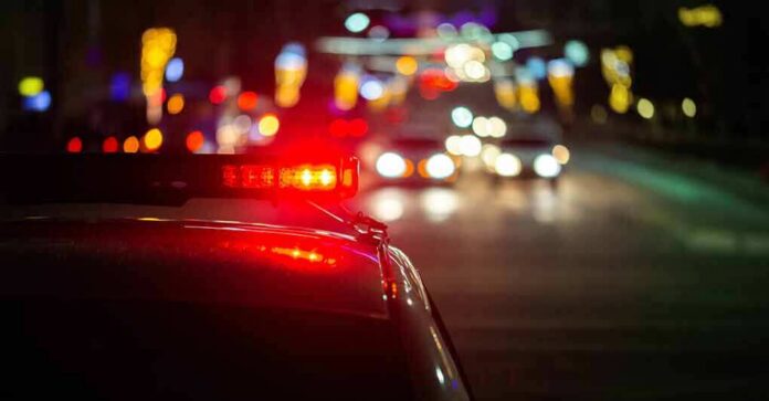 shutterstock_1739802671 Police car with flashing red lights on a city street at night