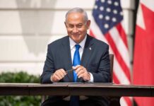 UN Erupts As Netanyahu Crowns Trump man in a suit sitting at a table with flags in the background