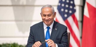 man in a suit sitting at a table with flags in the background