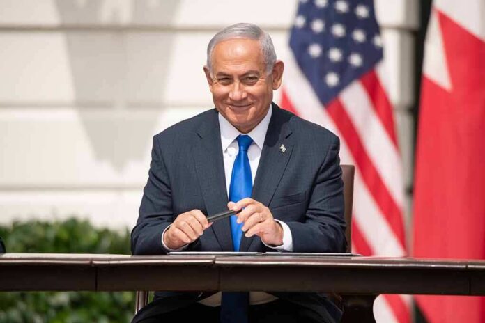 man in a suit sitting at a table with flags in the background