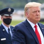 Donald Trump walking outdoors with an officer behind him; Chuck Howley not visible