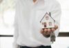ICE Raids Tied To Rent Slide? Hand holding a small house model and house-shaped key