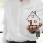 Hand holding a small house model and house-shaped key