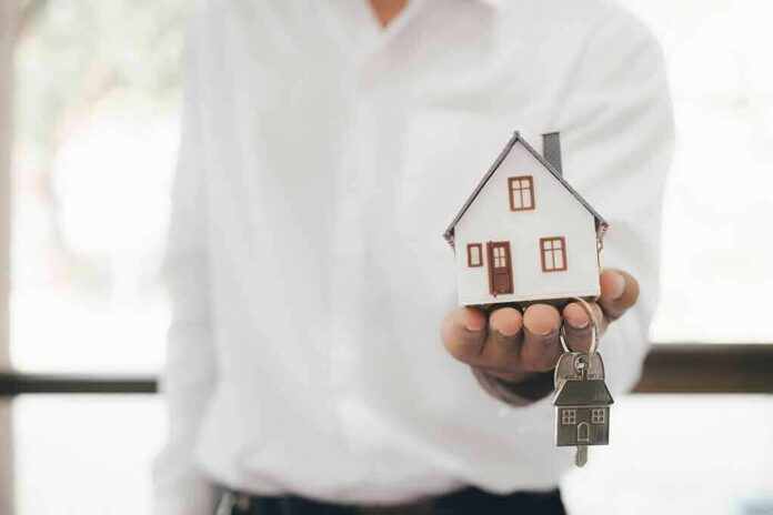 Hand holding a small house model and house-shaped key