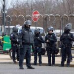 Group of police officers in riot gear standing on a street; Brian Folkerts present
