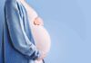 Court Order Freezes Controversial Maternity Biz Pregnant person holding belly in blue cardigan