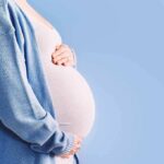 Pregnant person holding belly in blue cardigan