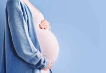 Court Order Freezes Controversial Maternity Biz Pregnant person holding belly in blue cardigan