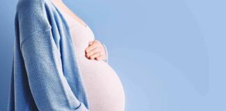 Pregnant person holding belly in blue cardigan