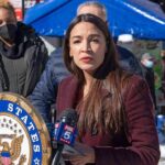 Prime-Time Swipe Targets AOC’s Fertility Woman speaking at outdoor press event with microphones and seal