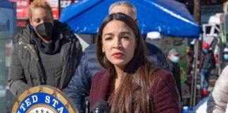 Woman speaking at outdoor press event with microphones and seal