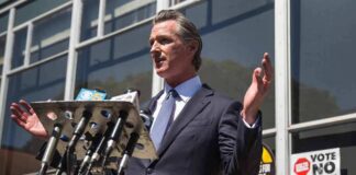 Gavin Newsom speaks at a press conference with microphones outside a building