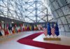 Row of national flags in a modern glass atrium with red carpet and EU and US flags upfront