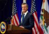 Newsom Signals A Shift On Supreme Court Man in suit speaking at a podium with American and California flags