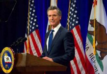 Newsom Signals A Shift On Supreme Court Man in suit speaking at a podium with American and California flags