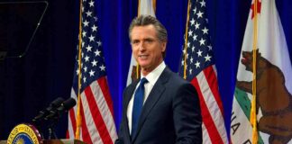 Man in suit speaking at a podium with American and California flags