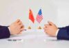 Trump – Xi Pause Dodges Pain, For Now Two diplomats sit across table with China and United States flags between them